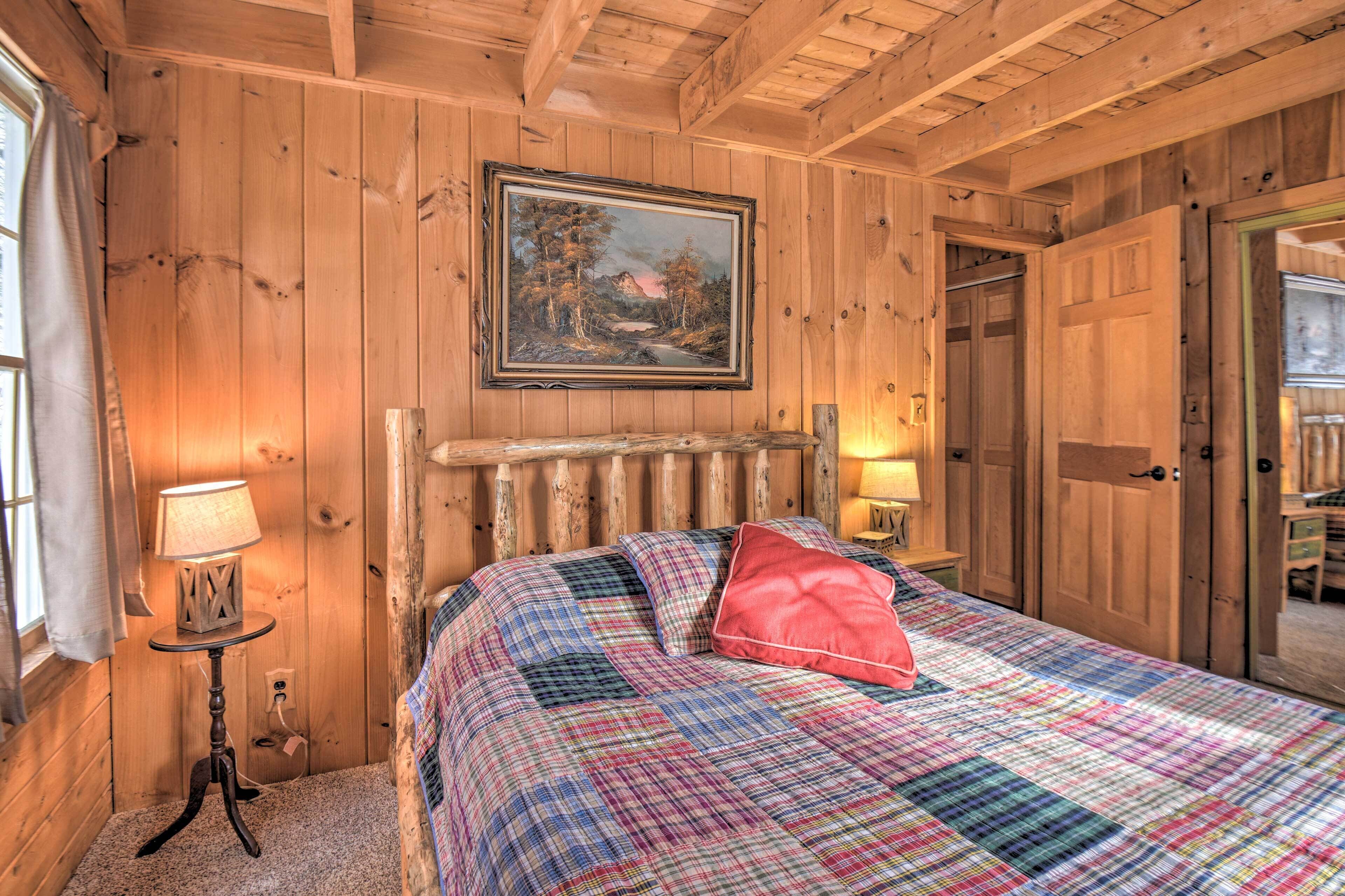 Un dormitorio de cabaña de madera con una cama, un cuadro y una puerta que da a otra habitación.