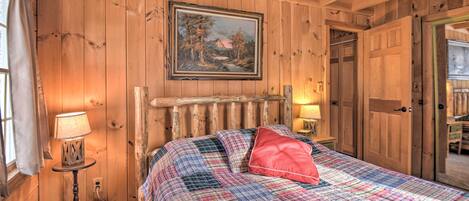 Un dormitorio de cabaña de madera con una cama, un cuadro y una puerta que da a otra habitación.