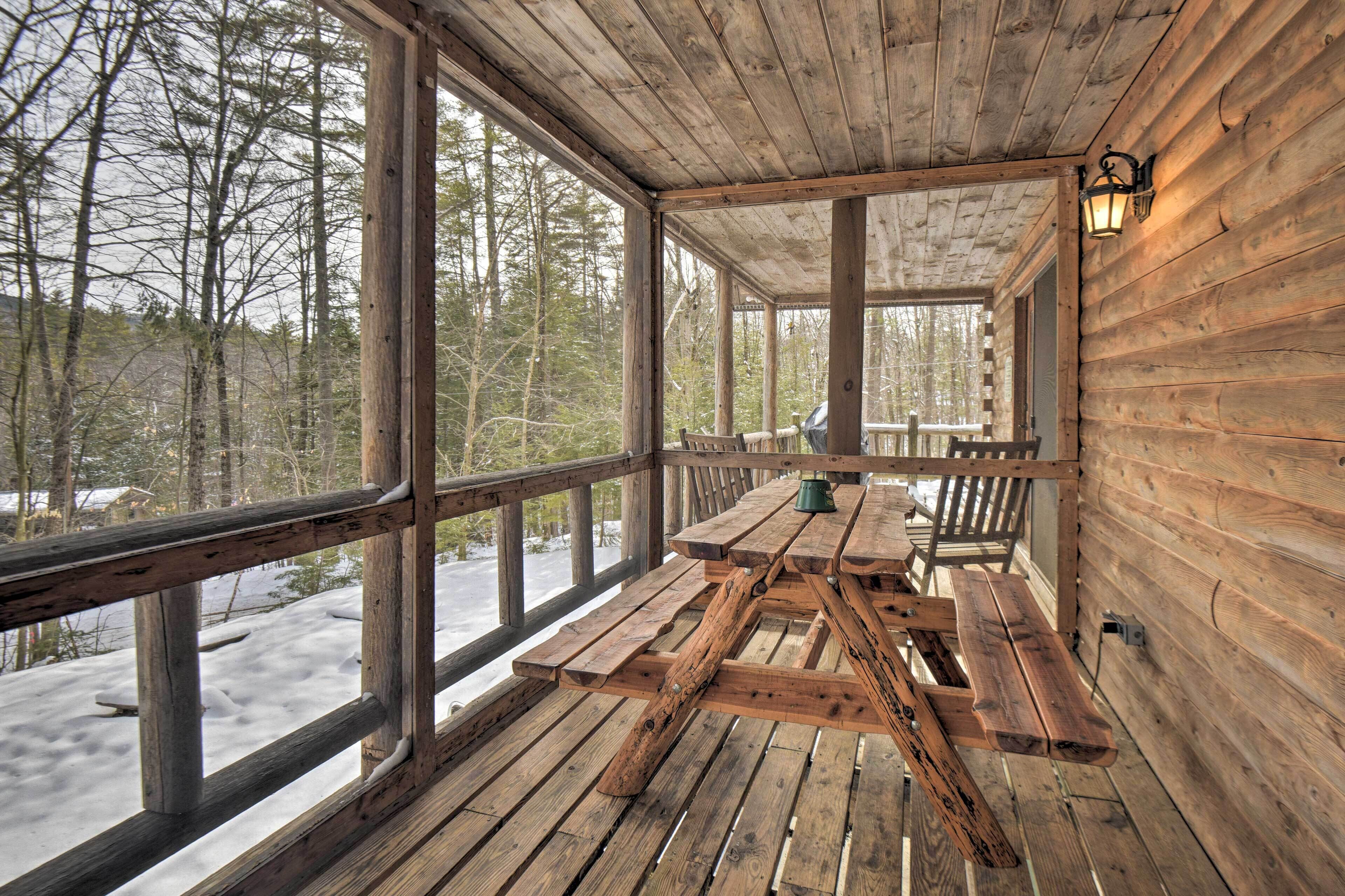 A wooden deck with a picnic table and benches, surrounded by a wooden cabin with large windows.