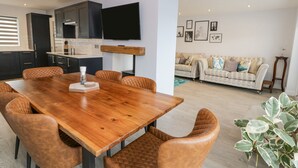 Un espace de vie moderne comprenant une table à manger en bois, des fauteuils en cuir, un coin cuisine, un téléviseur à écran plat et un coin salon confortable avec un canapé à motifs.