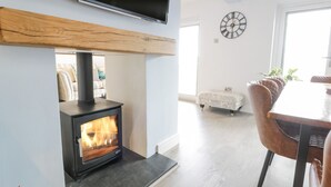 Un salon moderne avec un poêle à bois, un coin repas avec des fauteuils en cuir et une grande horloge au mur.