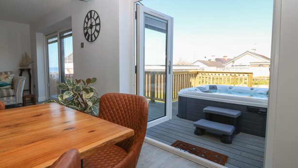 Une terrasse avec une table et des chaises en bois, un jacuzzi et une vue sur le jardin.