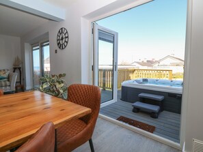 A patio with a wooden table and chairs, a hot tub, and a view of the backyard. - Melody (Cemaes Bay)