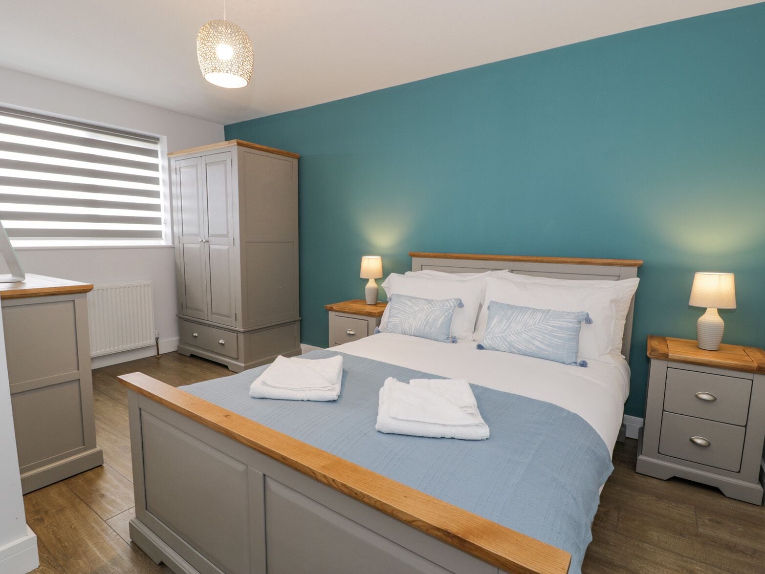 A bedroom with a bed, two bedside tables, a wardrobe, and a window with blinds.