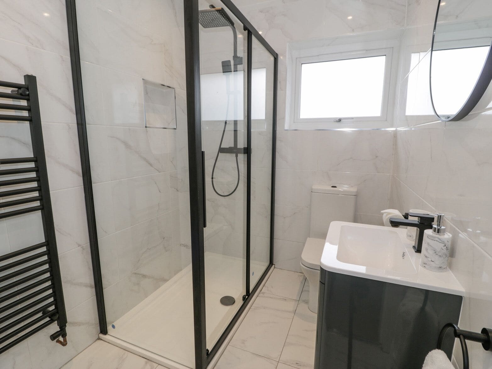A modern bathroom with a glass-enclosed shower, a white sink with a marble countertop, and a black towel rack.