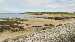 Une plage côtière avec un rivage rocheux, un ciel dégagé et une colline visible au loin.