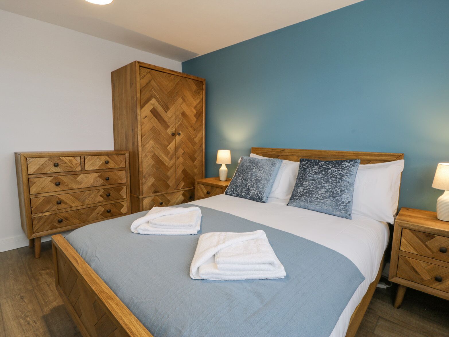 Un dormitorio con cama, armario de madera, mesitas de noche y pared azul.