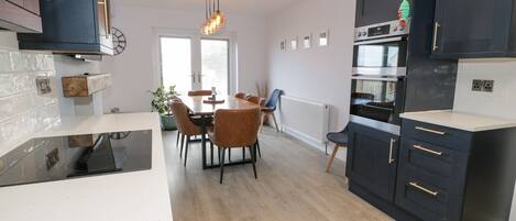 Eine moderne Küche mit dunklen Schränken, ein Essbereich mit Holztisch und Stühlen sowie ein sichtbarer Heizkörper.