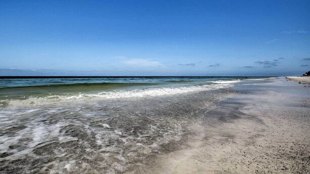 A beach with clear water, a sandy shore, and a clear sky.