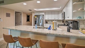 A modern kitchen with a central island, bar stools, stainless steel appliances, and white cabinetry.