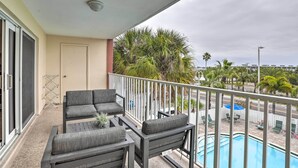 A balcony with a pool, outdoor seating, and palm trees.