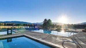 Piscina con vistas despejadas a montañas al fondo, rodeada por un área vallada con sillas de descanso.