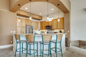 A kitchen with wooden cabinets, a stainless steel refrigerator, a microwave, and a bar area with four bar stools. - Fraser Townhome w/ Deck, 7 Mi to Winter Park! (Fraser)