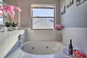 A bathroom with a bathtub, a window, and a vase with flowers.