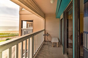 Ein Balkon mit Blick auf den Strand, ein kleiner Tisch und eine Bank.