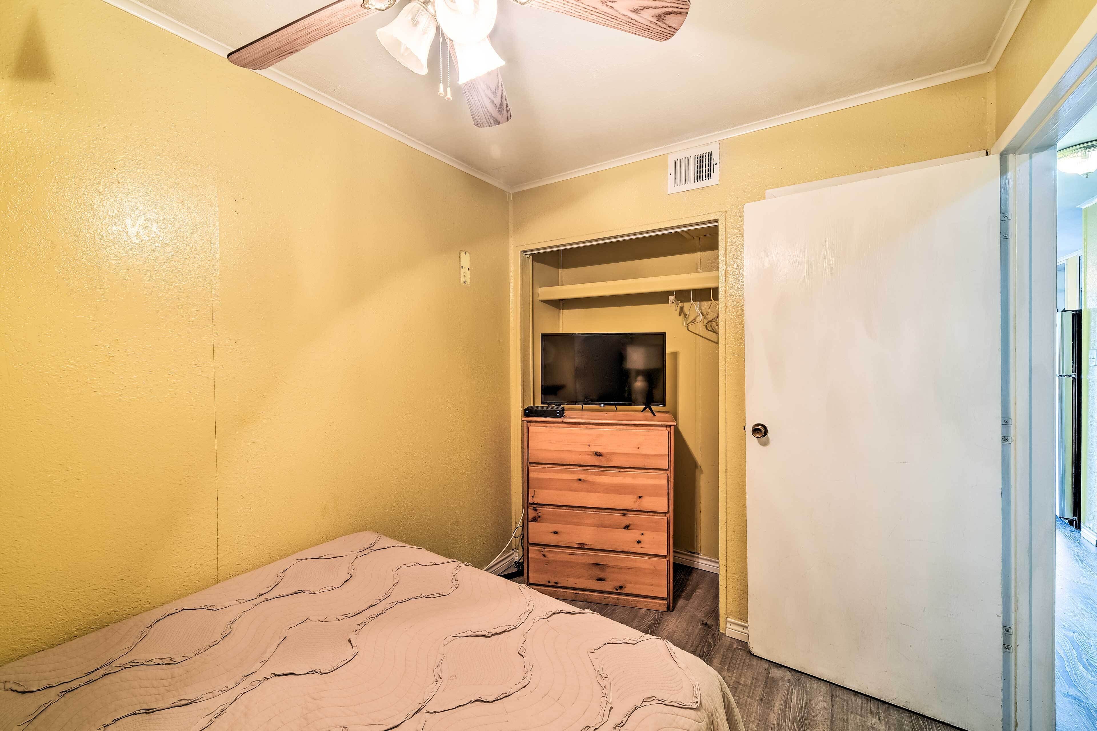 A bedroom with a bed, a wooden dresser, a door, and a ceiling fan.