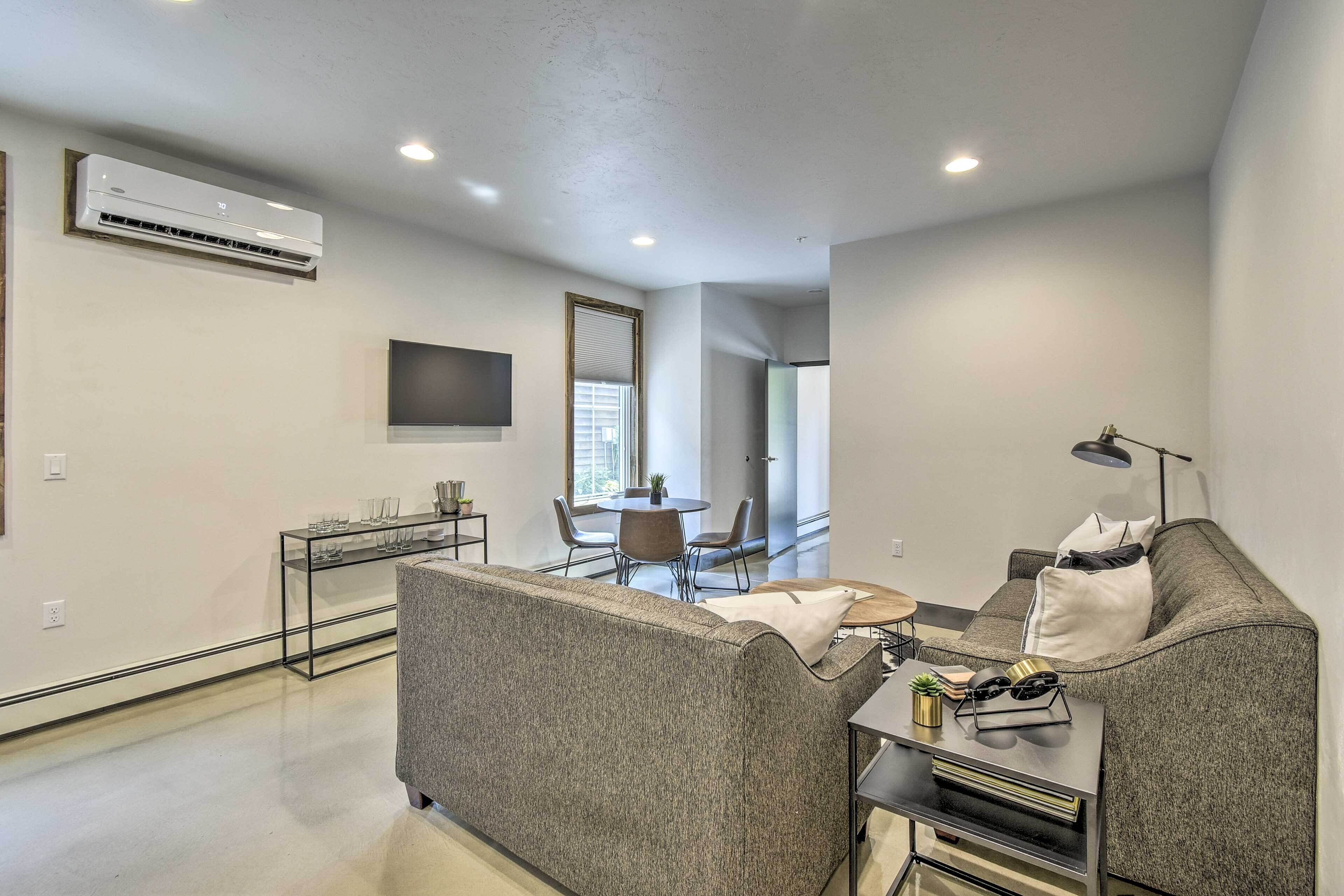 A modern living room with a grey sofa, a small side table, and a flat-screen TV mounted on the wall.