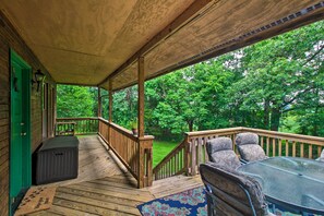Une terrasse en bois avec une table et des chaises en verre, une porte verte et une vue sur un paysage verdoyant.