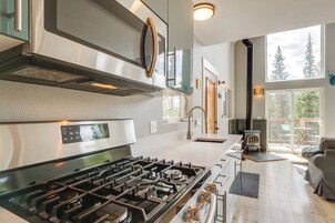 A modern kitchen with a stainless steel stove, a built-in oven, and a large window overlooking a deck.
