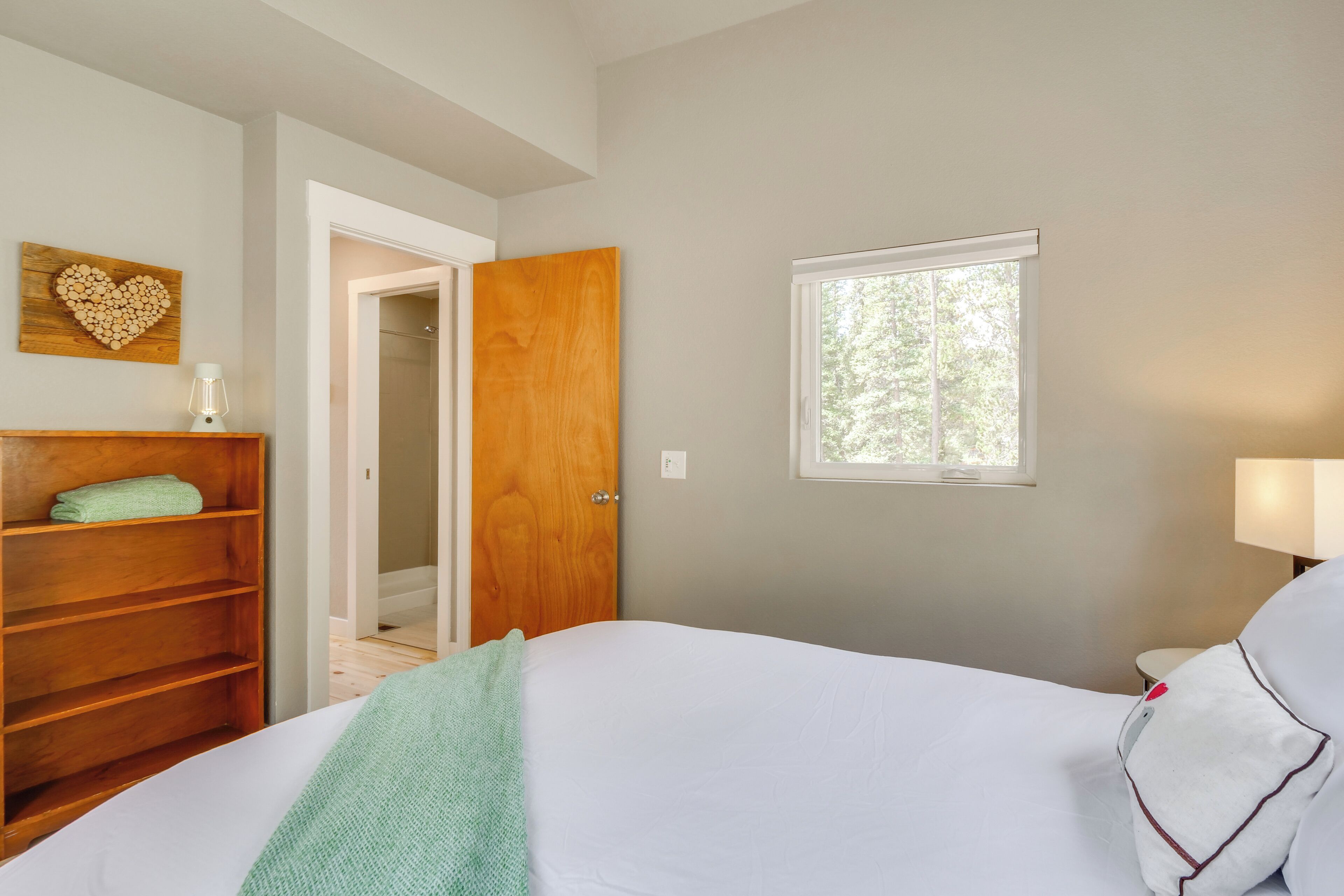 Un dormitorio con una cama, un armario de madera, una decoración en forma de corazón en la pared, una ventana y una puerta que da a otra habitación.