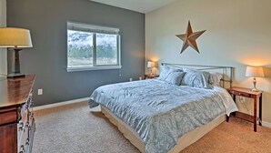 A bedroom with a large bed, two bedside tables with lamps, a star decoration on the wall, and a window with a view of trees. - Prime Snowy Retreat Mins to Tamarack & Mccall! (Donnelly)