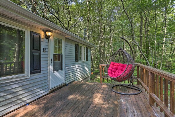 Une terrasse en bois avec un fauteuil suspendu et une maison dotée d’un porche.