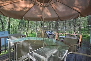 An outdoor deck with glass tables and chairs, a barbecue grill, and a large umbrella providing shade. - North Arrowhead Lake Cabin w/ Deck, Pets Welcome! (Pocono Lake)