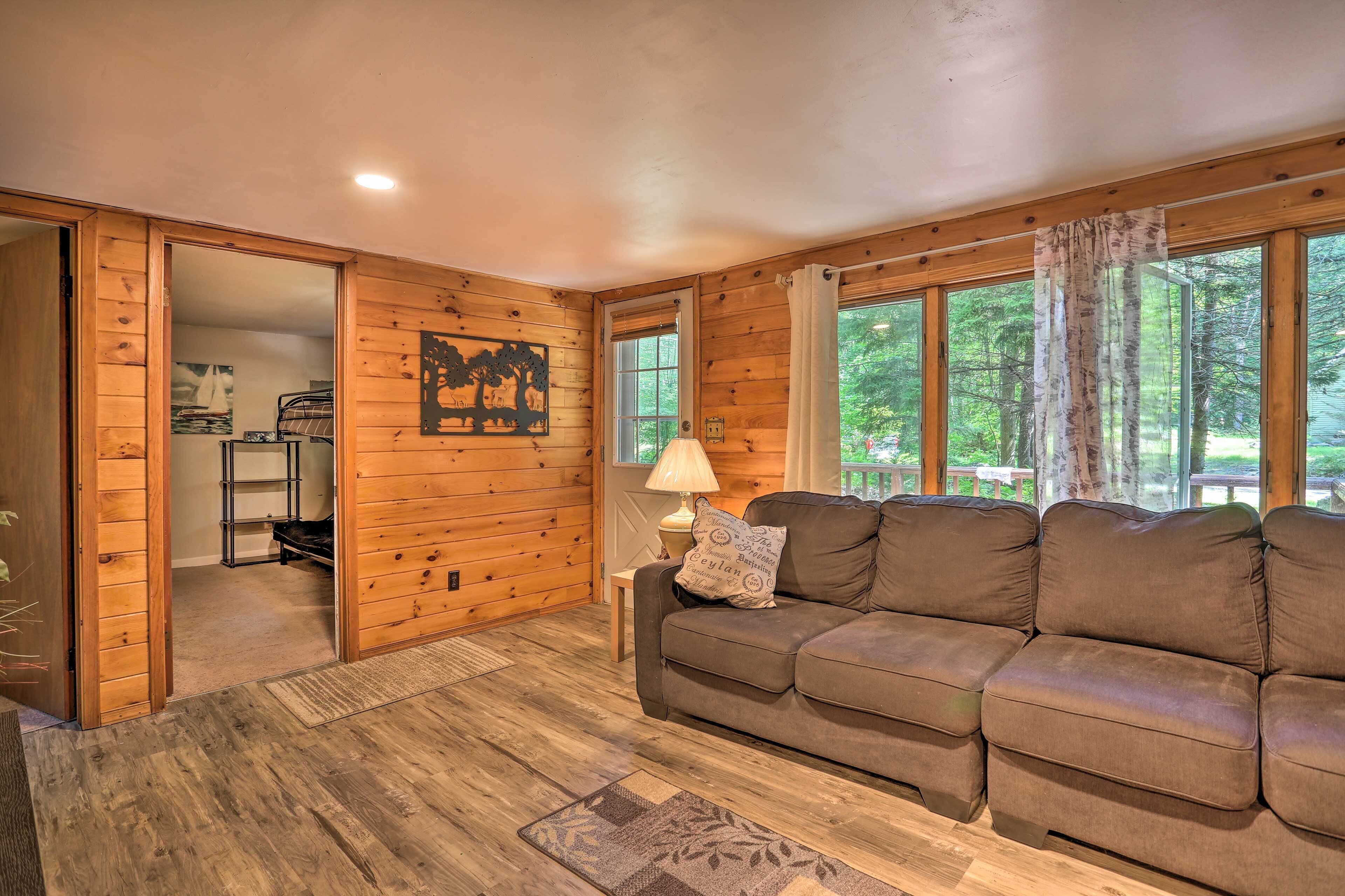 A cozy cabin interior with a wooden floor, a brown sectional sofa, a lamp, and a painting on the wall.