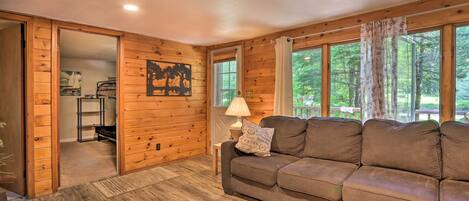 A cozy cabin interior with a wooden floor, a brown sectional sofa, a lamp, and a painting on the wall.
