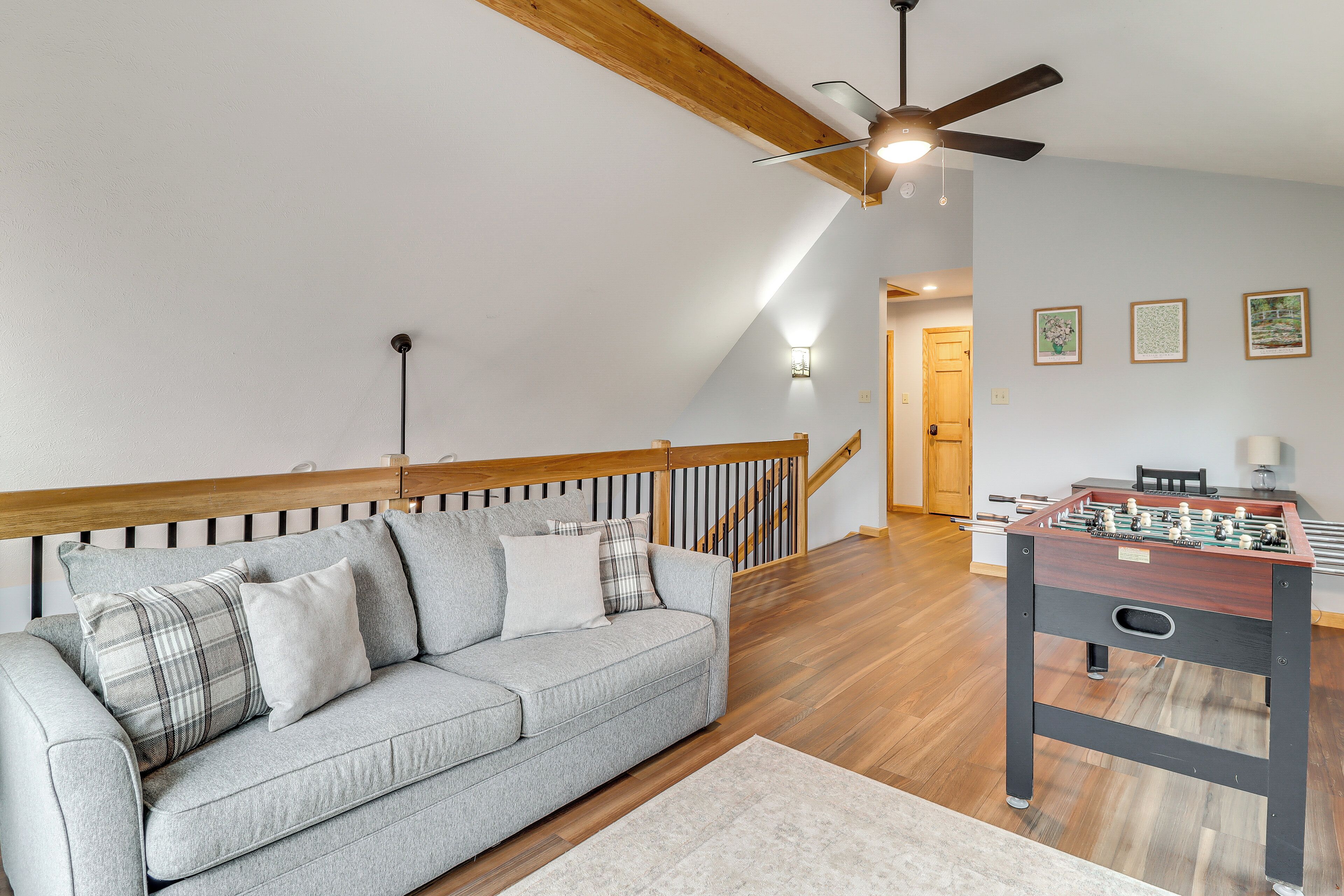 Een loft-kamer met een grijze bank, houten balken in het plafond, een plafondventilator en een tafelvoetbaltafel.