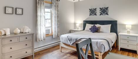 Un dormitorio con cama, mesitas de noche, cómoda, ventilador de techo y ventana con cortinas.