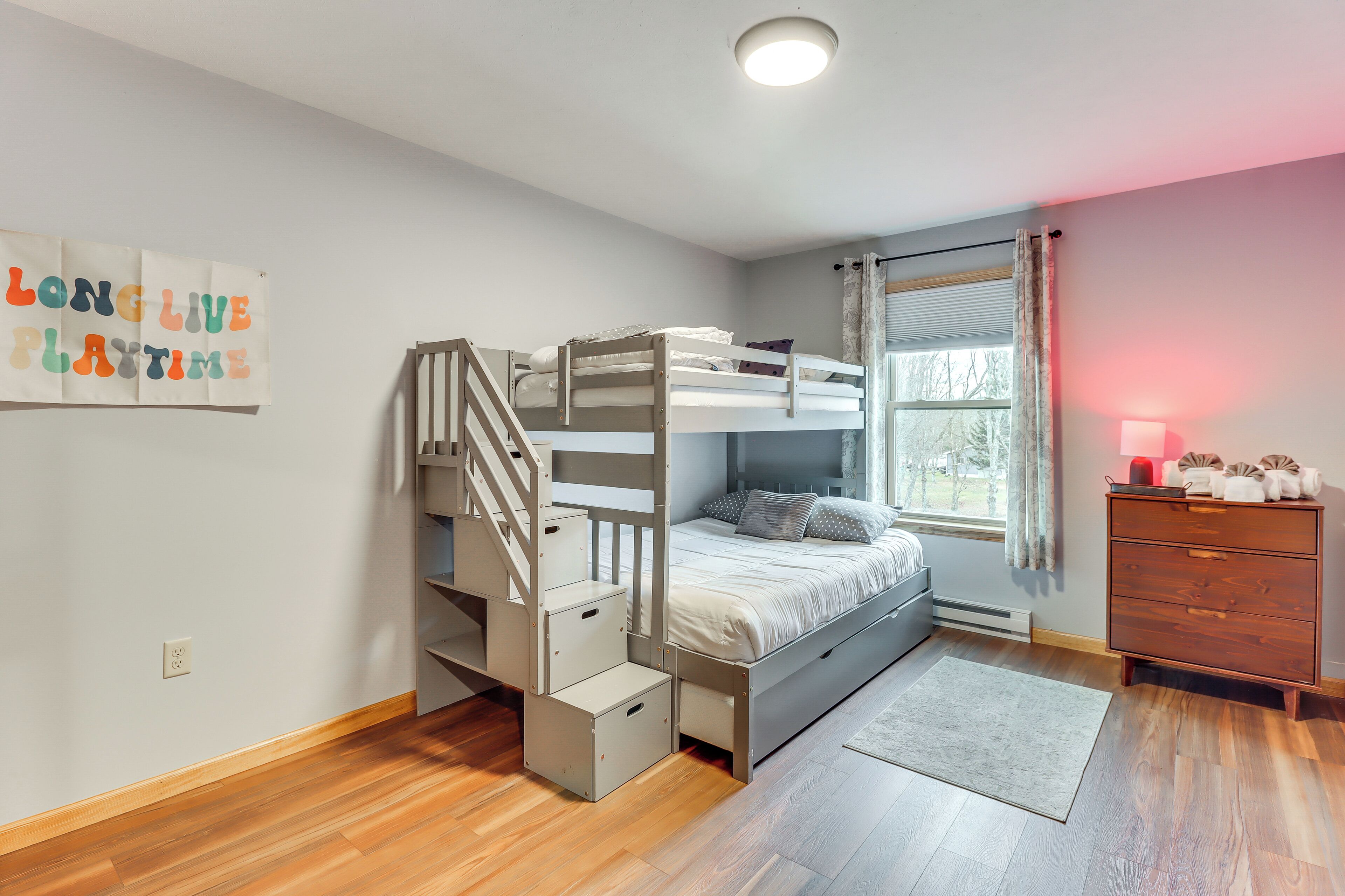 Um quarto com uma cama beliche, escada de madeira, cômoda e janela com cortinas.