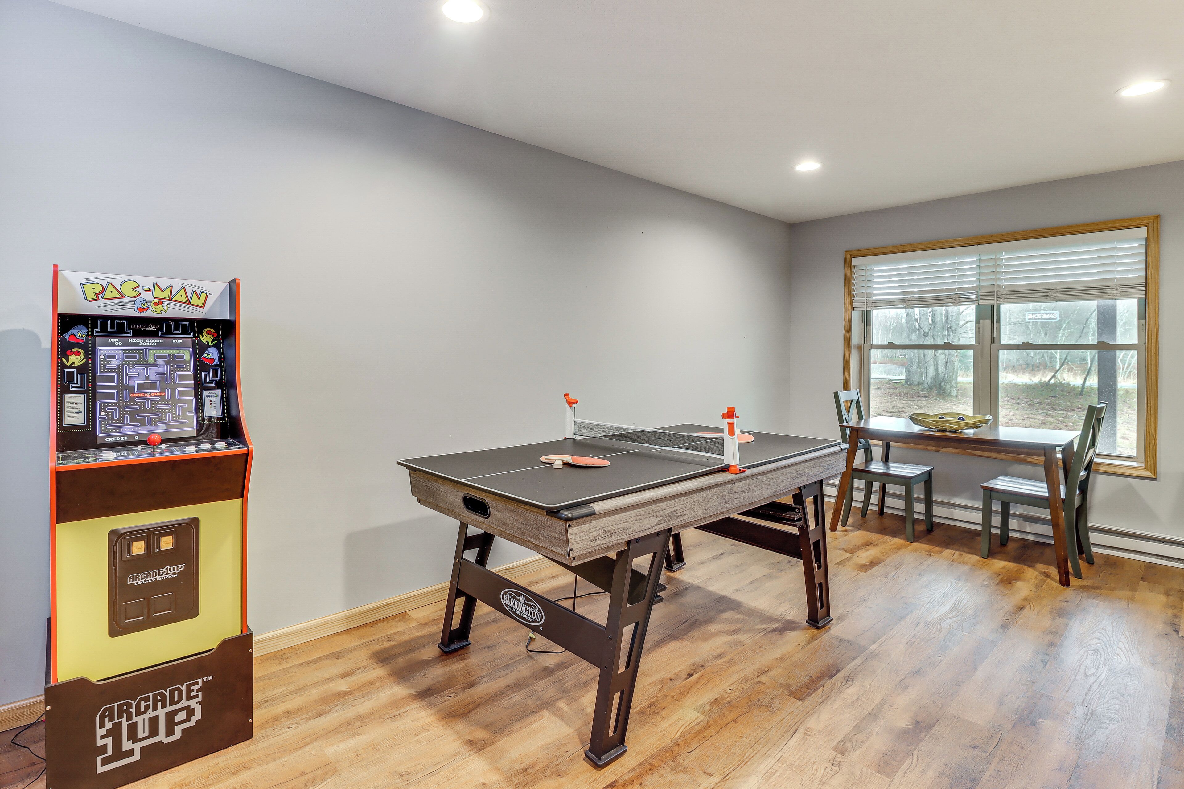 Une pièce équipée d’une table de ping-pong, d’une borne d’arcade Pac-Man et d’un coin repas avec une fenêtre.