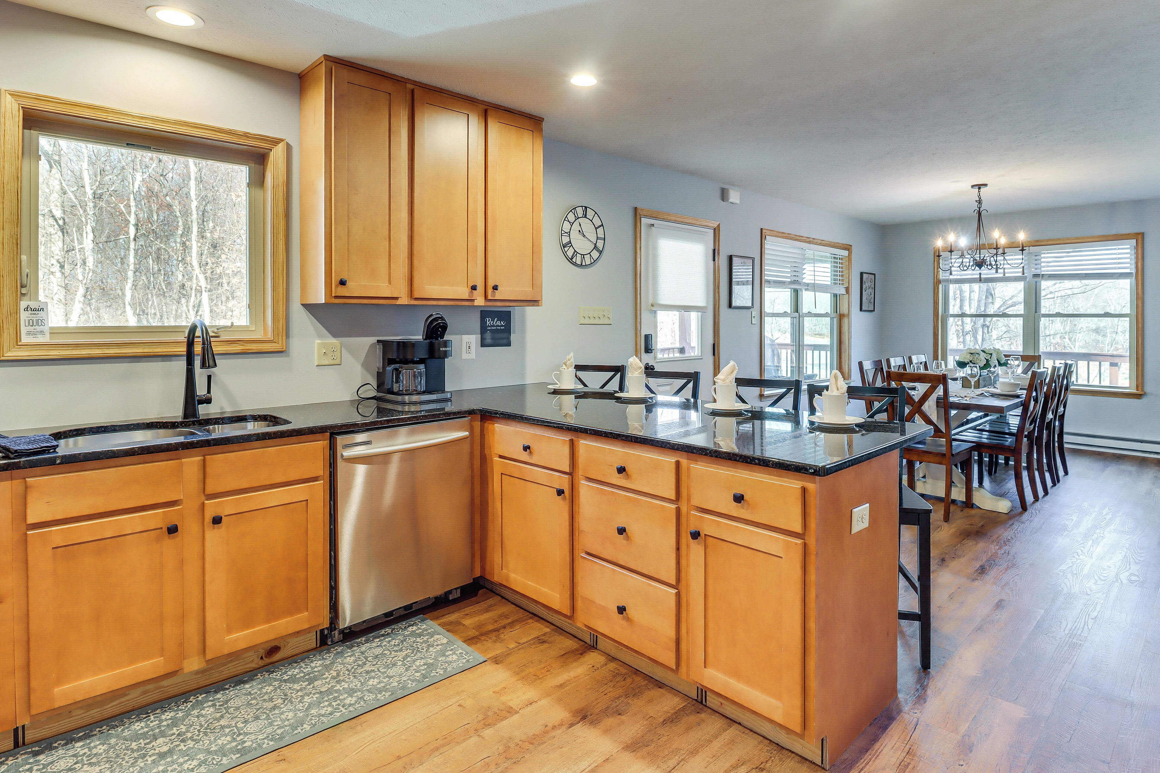 A kitchen with wooden cabinets, a stainless steel dishwasher, and a dining area with a chandelier.