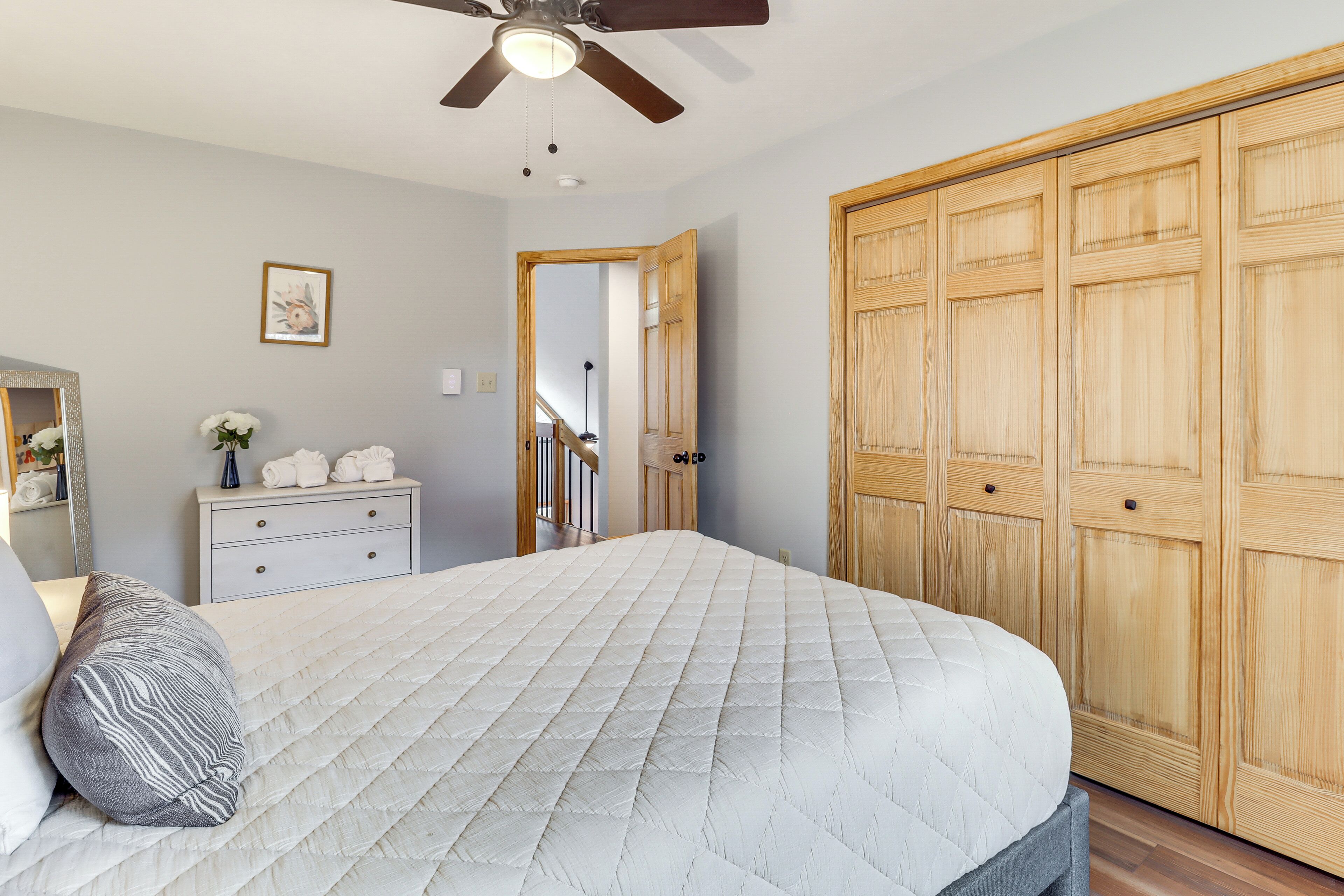 Un dormitorio con cama, cómoda, espejo, ventilador de techo y armario.