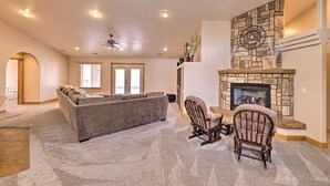 A spacious living room with a stone fireplace, a large grey sectional sofa, and two rocking chairs. - Hurricane Home w/ Pool & Spa ~ 25 Mi to Zion! (Hurricane)