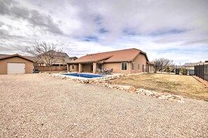 A residential property with a swimming pool, a covered patio, and a gravel driveway.