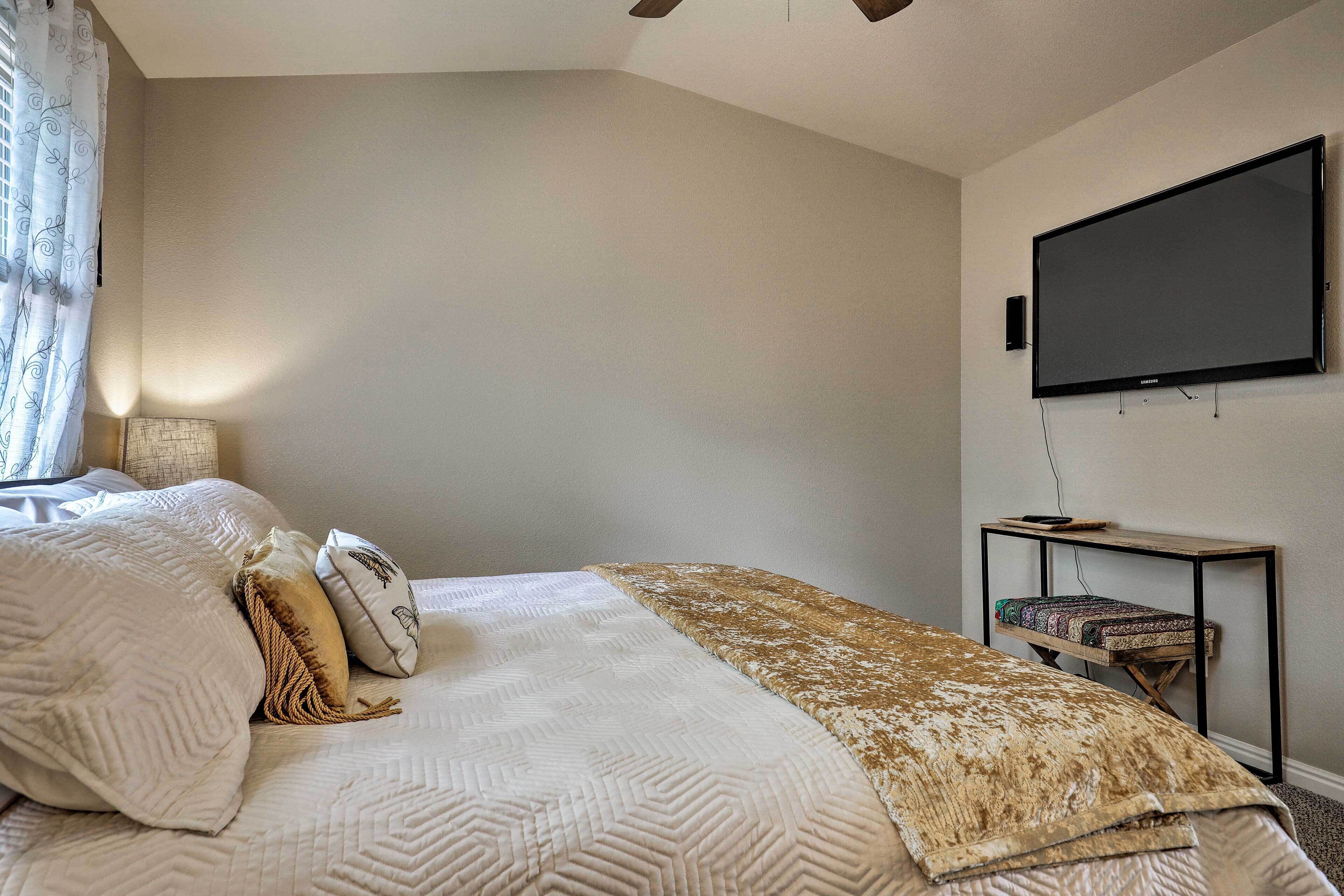 Un dormitorio con una cama, un televisor montado en la pared y una pequeña mesa con una silla.