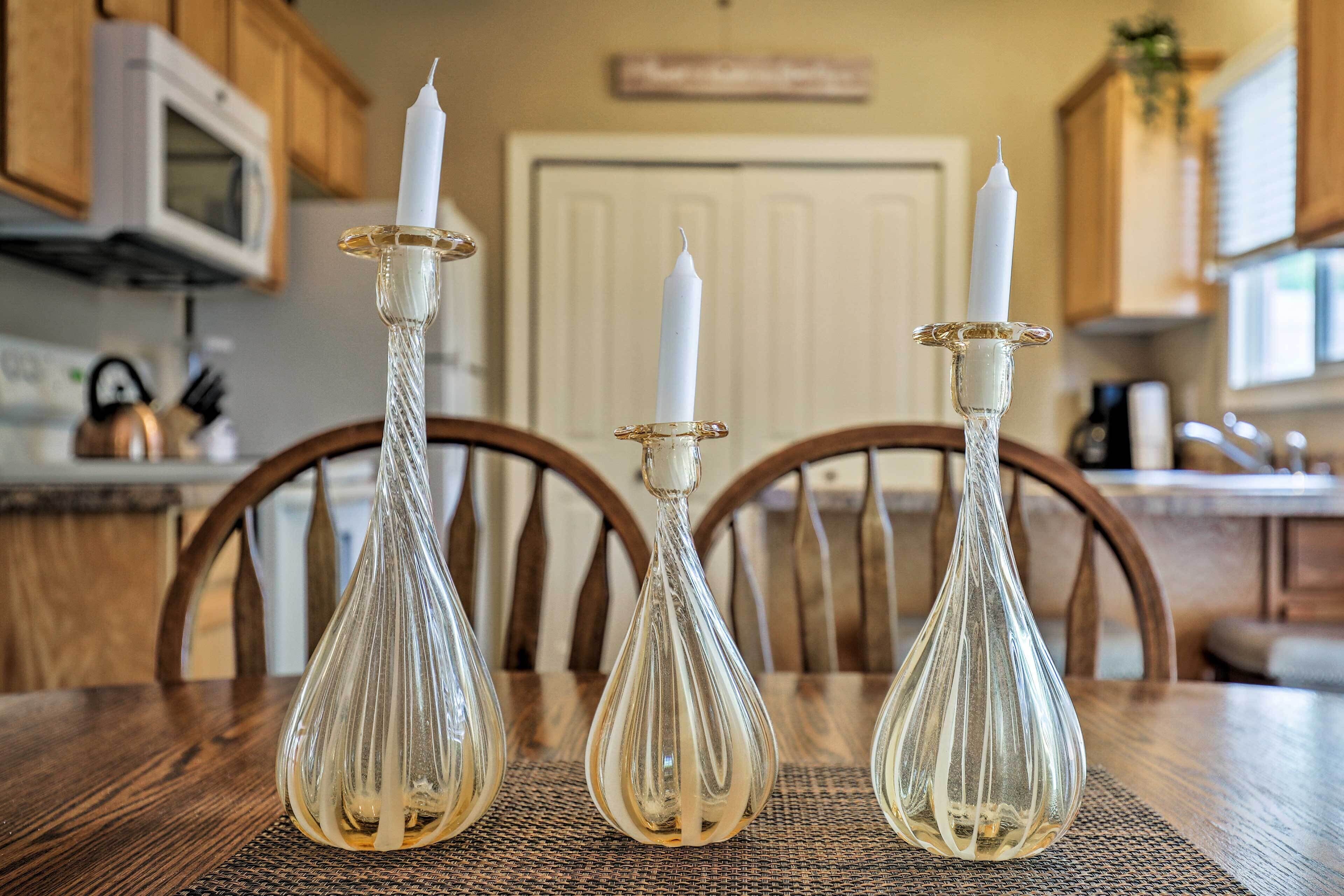 Tre portacandele in vetro con candele bianche su un tavolo di legno in una cucina.