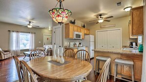 A dining area with a wooden table and chairs, a chandelier, and a kitchen in the background. - Lovely Kanab Condo in Dwtn, 30 mi to Zion NP! (Kanab)