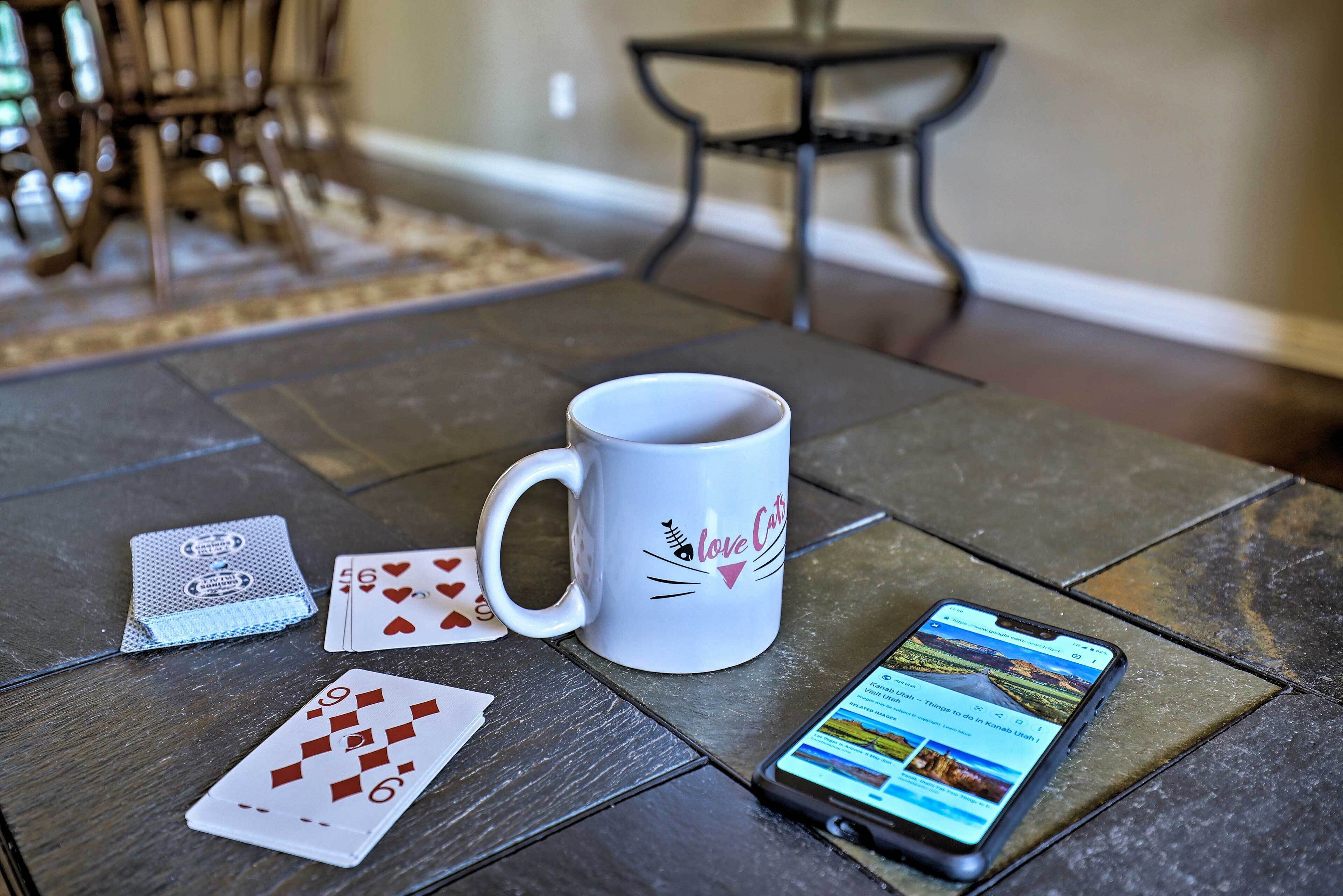 Een tafel met een witte mok, speelkaarten en een smartphone waarop een reisapp staat.