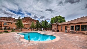 A pool area with a curved pool, surrounded by buildings with a stone facade and a mountain backdrop. - Lovely Kanab Condo in Dwtn, 30 mi to Zion NP! (Kanab)