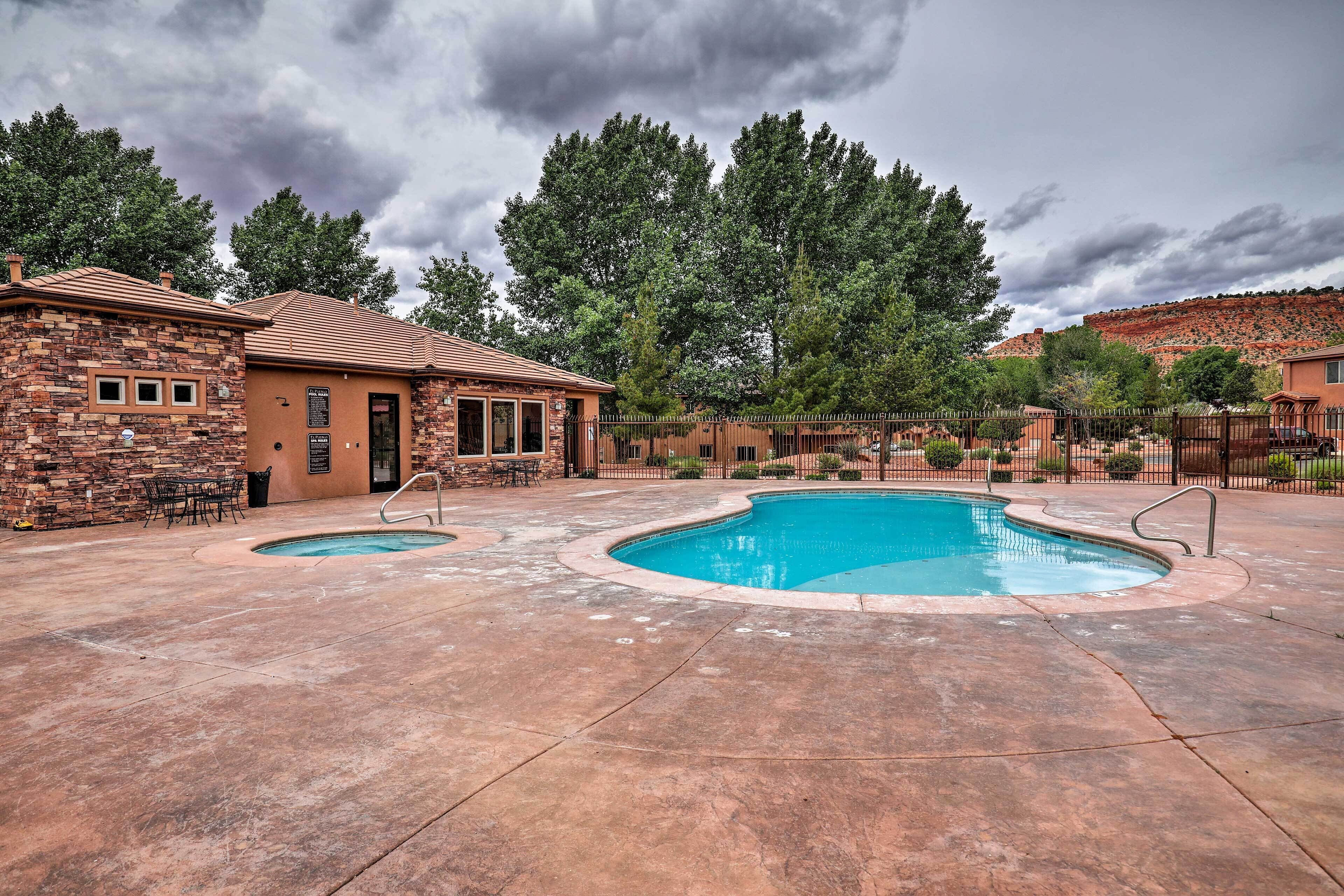 A backyard with a swimming pool, a brick building, and a fenced area with trees.