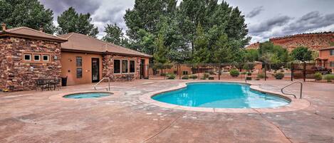 A backyard with a swimming pool, a brick building, and a fenced area with trees.