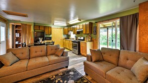 A living room with two sofas, a dining table, and a kitchen area with wooden cabinets and a large window. - Peaceful, Quiet Seward Apt W/back Yard & Mtn Views (Seward)