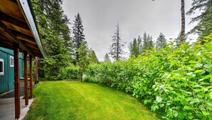 A well-maintained lawn with a wooden deck and a green building in the background. - Peaceful, Quiet Seward Apt W/back Yard & Mtn Views (Seward)
