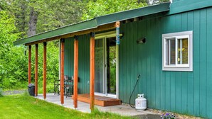 A green building with a covered porch, a sliding glass door, and a small window with shutters. - Peaceful, Quiet Seward Apt W/back Yard & Mtn Views (Seward)