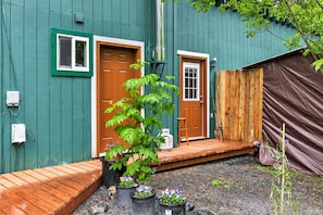 A green house with two doors, a wooden deck, and potted plants. - Peaceful, Quiet Seward Apt W/back Yard & Mtn Views (Seward)