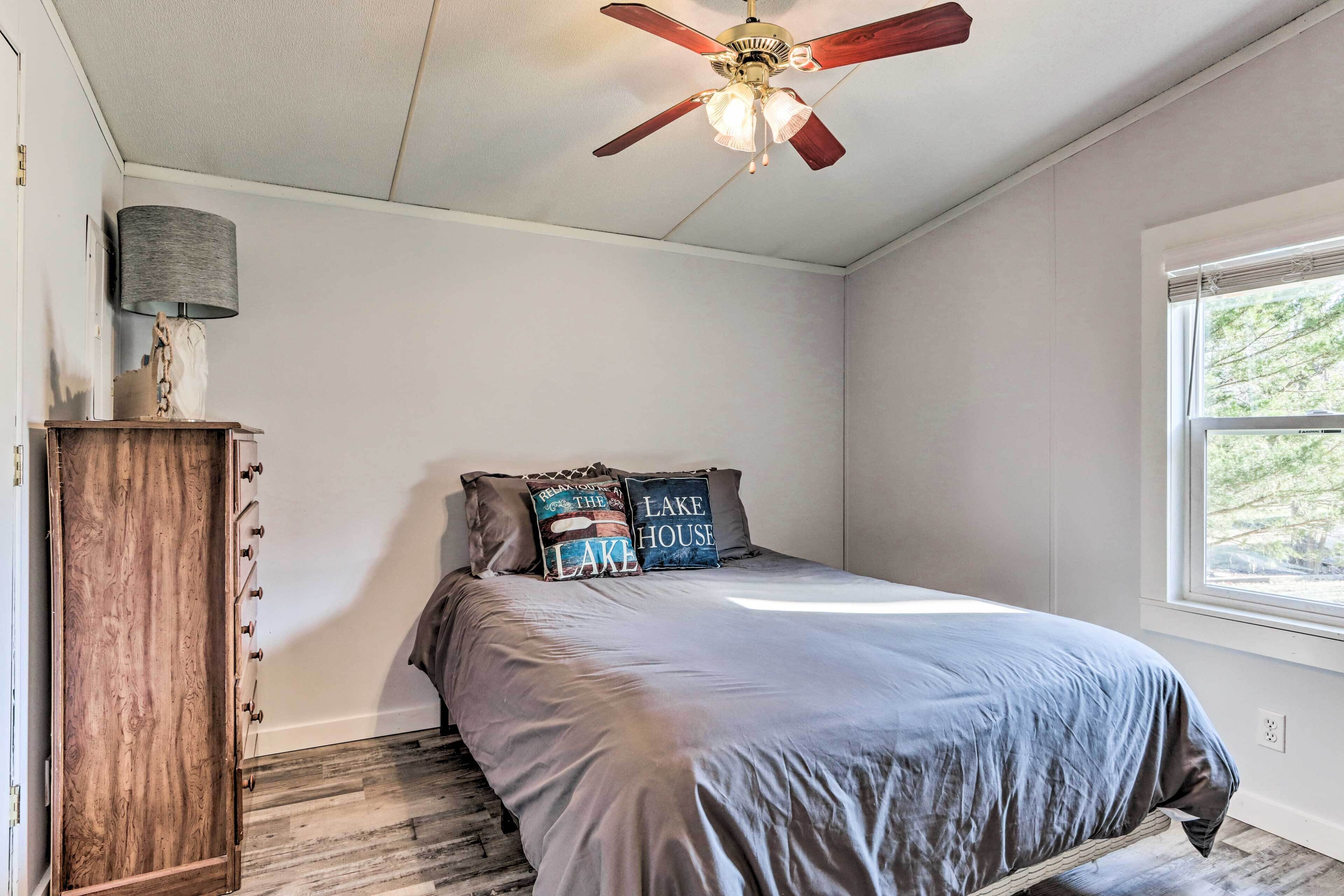 A bedroom with a bed, a ceiling fan, a lamp, and a window.