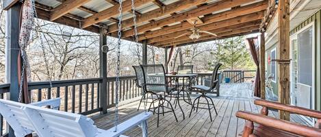 A covered outdoor deck with wooden furniture, including a swing, a table with chairs, and a bench.